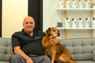 A middle-aged man sits on a couch with a brown dog.